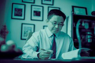 duotone photo of Tony Hu working on paper