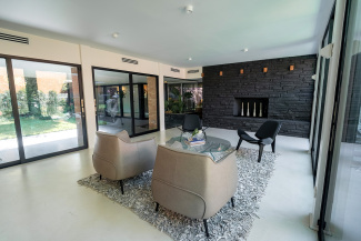 Modern living room with neutral tones, featuring two beige armchairs, a glass coffee table, and textured gray rug. A black stone fireplace adds elegance.
