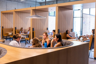 People collaborate at wooden booths in a modern space with natural light. The setting is relaxed, with open laptops and focused conversations.