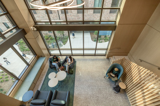 Spacious lobby with large windows, students studying on comfy chairs. Modern, airy interior with natural light and a relaxed atmosphere.