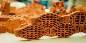 Close-up of interlocking 3D-printed clay structures on a white surface. The intricate lattice design in warm earthy tones evokes creativity and innovation.