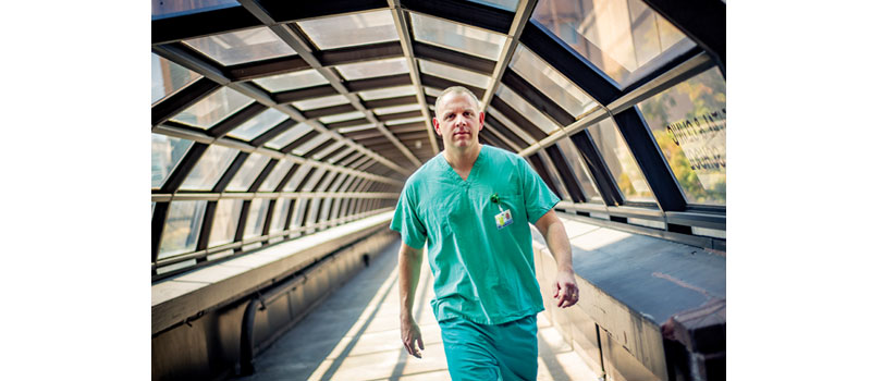 Dr. Josh Denson wears green scrubs as he strides across the bridge between Tulane medical school and hospital.