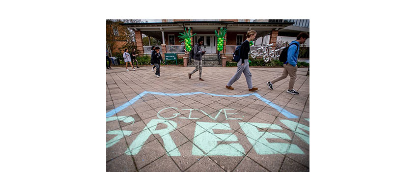 Student walk on concrete decorated with chalk that reads "Give Green."