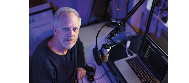 Nick Spitzer sits with a microphone, headphones and a computer