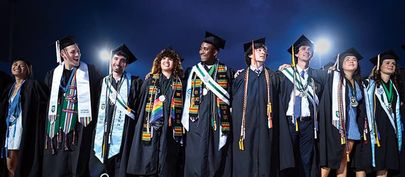 graduates in caps and gowns at the Commencement ceremony with night sky