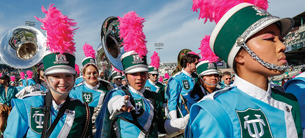 Tulane Marching Band members in blue and green uniforms with pink marching hat plumes