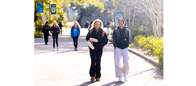 students walk through campus with sun behind them