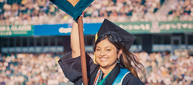 graduating woman carries gonfalon flag through a stadium