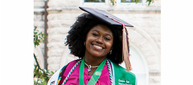 graduate Alexa Authorlee sits on the Tulane stone sign in front of Gibson Hall