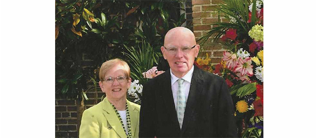 Gene and Mary Koss stand outside with flowers in the background