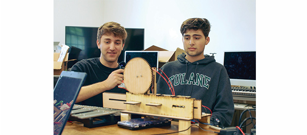 two students work to create a musical robot using wooden parts, computers, xylophone