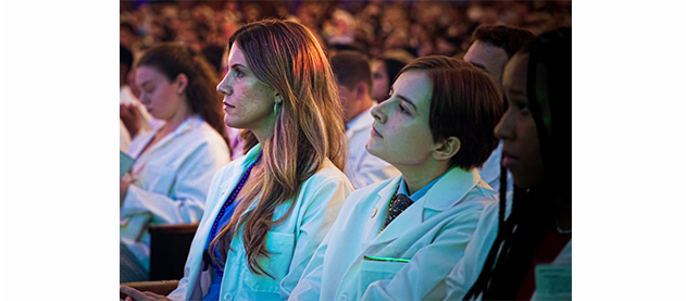 medical students wearing white coats are seated in an audience 