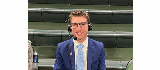 Isaac Popper wears broadcast headset while on the sidelines of a sports court