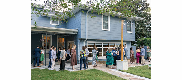 Guests gather outside at the a blue residential house for the dedication ceremony