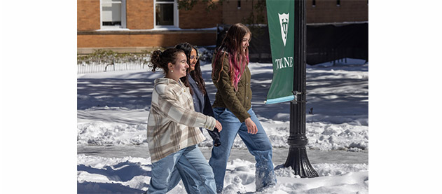 three students walk in snow on a sunny day on the Tulane campus