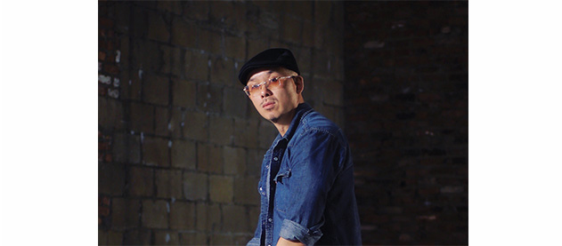 Bobby Yan wears a blue shirt and leans on a white armchair