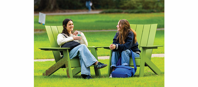 two students conversing outside in green chairs on a green lawn