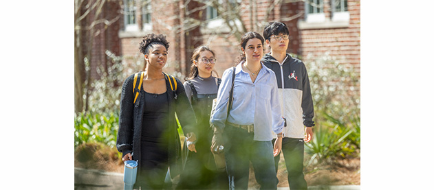 A cheerful group of four students walking outdoors, surrounded by greenery
