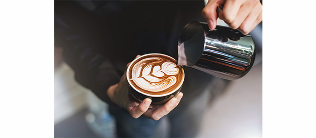 A person decorates a cup of coffee with steaming milk
