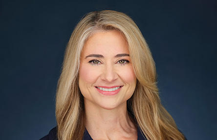 Portrait of Colette Hirstius. A woman with long, blonde hair smiles warmly against a dark blue background.