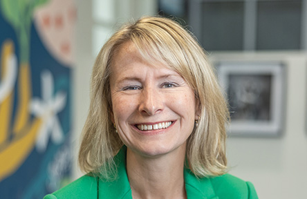 A portrait of Amelia Manning wearing a bright green blazer, photographed in an office setting.