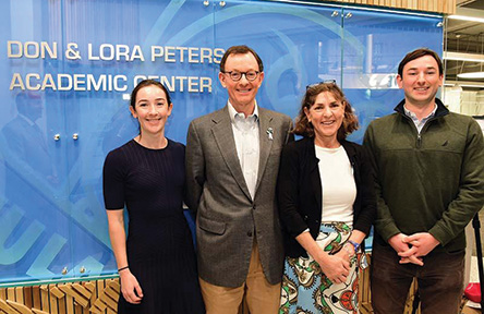 The Peters family: duaghter, father (Don), mother (Lora) and son stand in front of a blue sign that reads "Don & Lora Peters Academic Center".