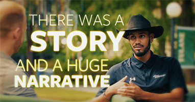 A man in a black hat and shirt gestures while speaking to another person outdoors. Text overlay reads, "There was a story and a huge narrative." The atmosphere is engaging.