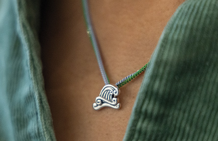 Colorful cord necklace with silver wave pendant on a person in a green shirt.