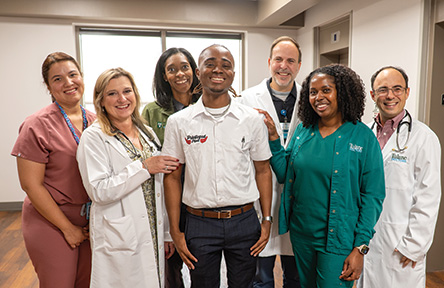 Seven smiling medical staff members and a young man in a white polo shirt.