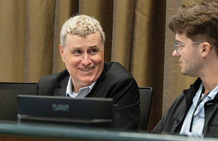 Smiling man with blond hair engages with another man in a meeting.