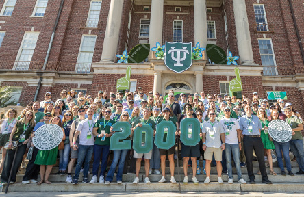 Group holding green "2000" in front of a university building with a logo.