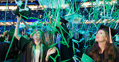 Streamers fall on graduates celebrating in a stadium.