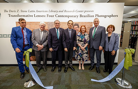 Seven people pose in front of a photography exhibition backdrop at a ribbon cutting.
