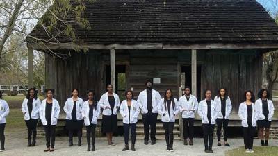15 Black medical school students in white coatspose in front of Whitney Plantaion