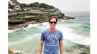 Zachary St. Martin stands in front of ocean wearing a "Defend New Orleans" T-shirt