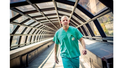 Dr. Josh Denson wears green scrubs as he strides across the bridge between Tulane medical school and hospital.