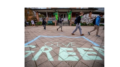 Student walk on concrete decorated with chalk that reads "Give Green."