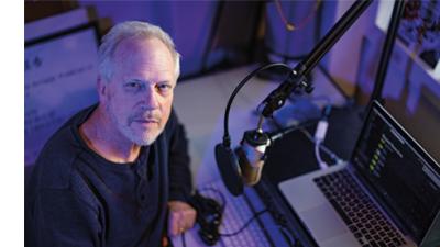 Nick Spitzer sits with a microphone, headphones and a computer