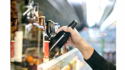 close up of hand reaching for a bottle on a grocery store shelf