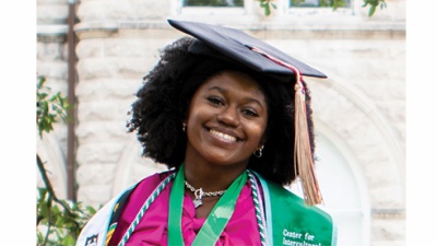 graduate Alexa Authorlee sits on the Tulane stone sign in front of Gibson Hall