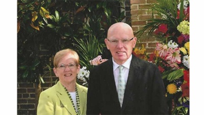 Gene and Mary Koss stand outside with flowers in the background