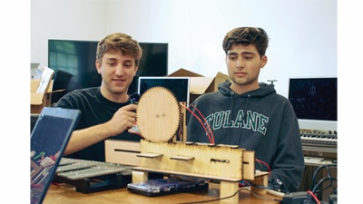 two students work to create a musical robot using wooden parts, computers, xylophone