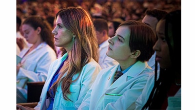 medical students wearing white coats are seated in an audience 