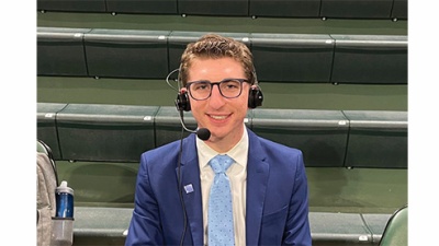 Isaac Popper wears broadcast headset while on the sidelines of a sports court