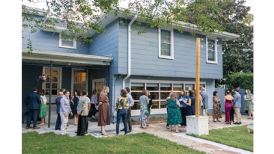 Guests gather outside at the a blue residential house for the dedication ceremony