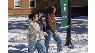 three students walk in snow on a sunny day on the Tulane campus