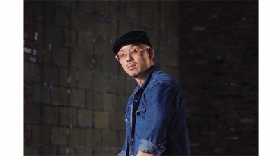 Bobby Yan wears a blue shirt and leans on a white armchair