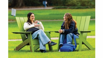 two students conversing outside in green chairs on a green lawn