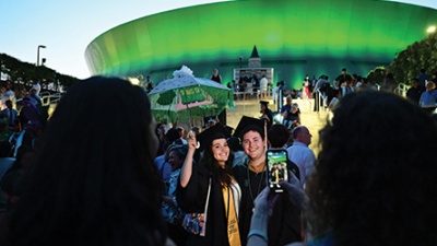 Graduates pose for photos with a green-lit Superdome TH graduates in cap and gown pose for a photo outside a green-lit Superdome at dusk, surrounded by a crowd of people
