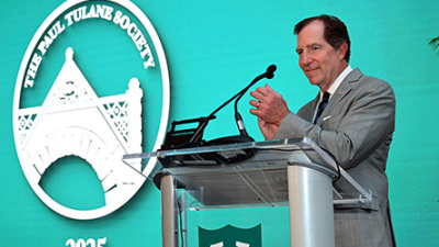 David Mussafer in a gray suit claps at a clear podium against a teal backdrop. The Paul Tulane Society logo and "2025" are displayed prominently.